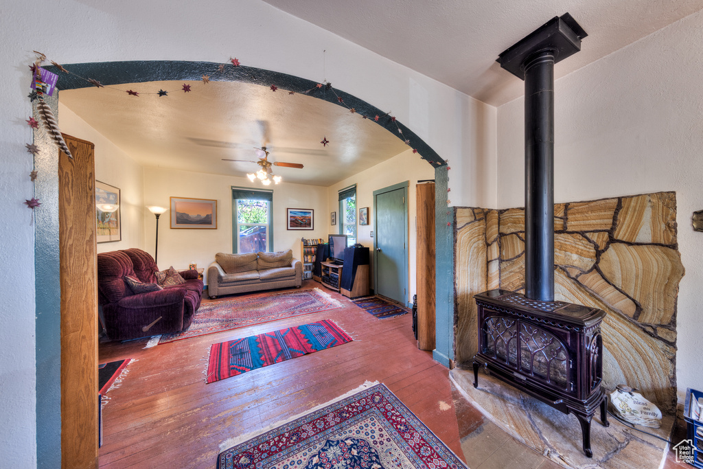 Living area with hardwood / wood-style floors, a wood stove, a ceiling fan, and arched walkways