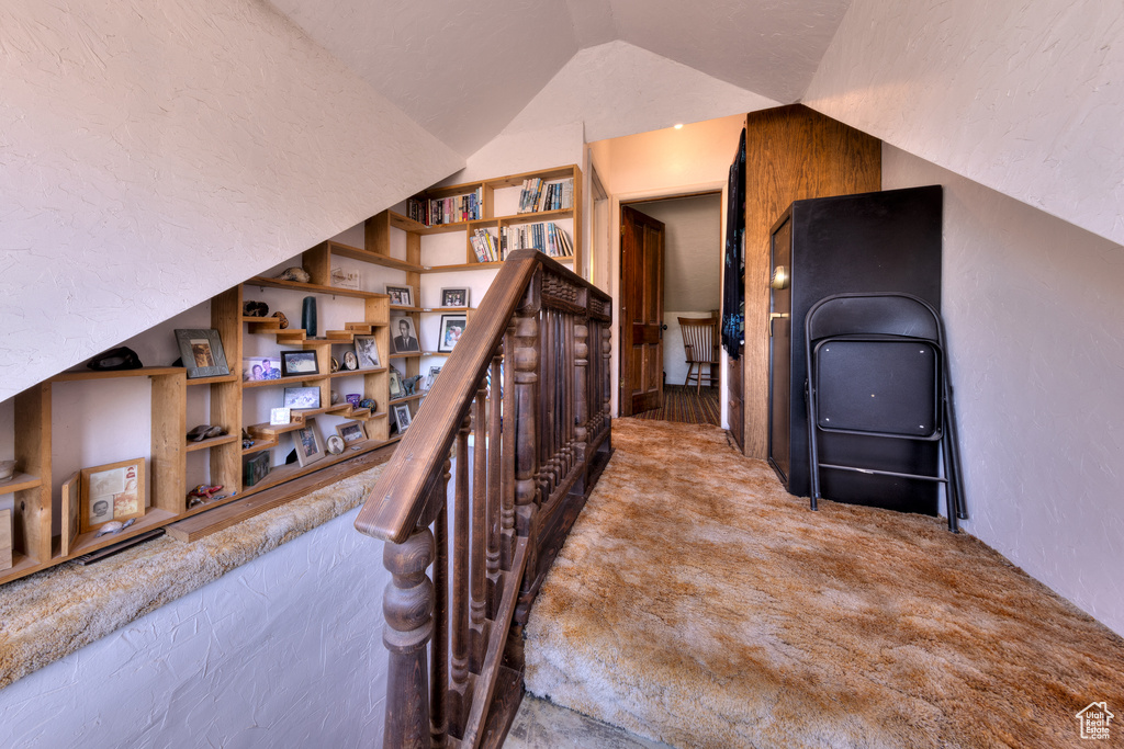 Hallway with built in features, carpet floors, an upstairs landing, and lofted ceiling