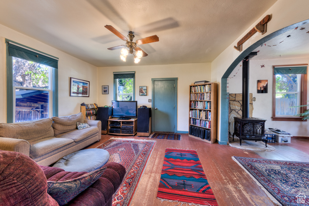 Living room featuring wood finished floors, ceiling fan, a wood stove, and healthy amount of natural light