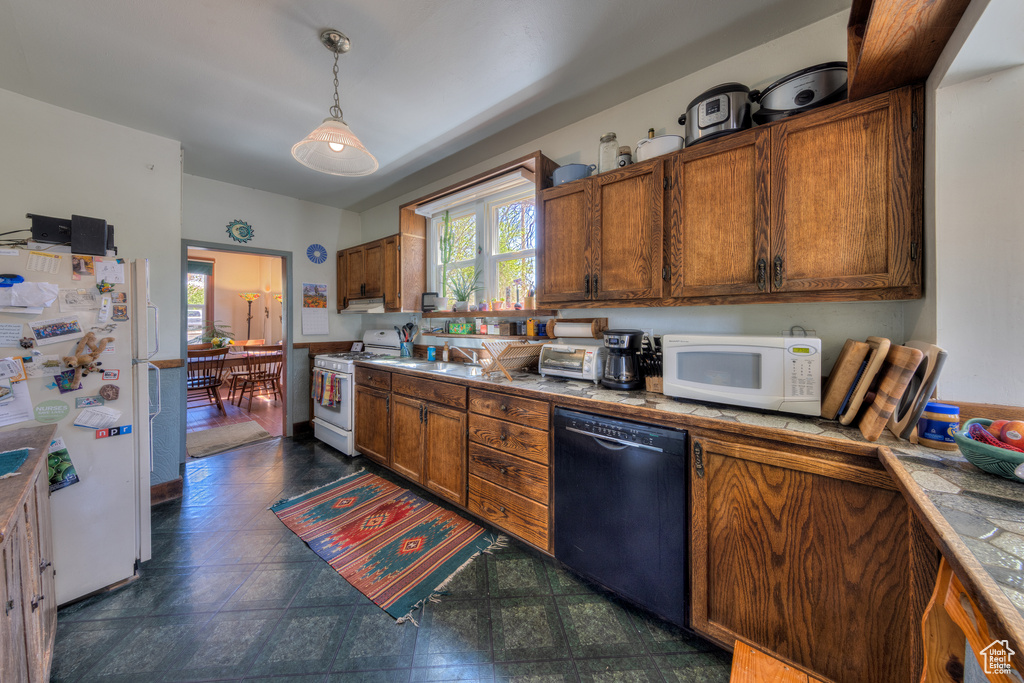 Kitchen featuring white appliances, plenty of natural light, brown cabinetry, and hanging light fixtures