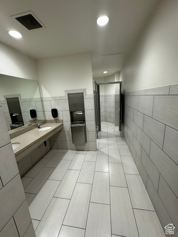 Full bathroom with double vanity, visible vents, tile walls, a stall shower, and a sink