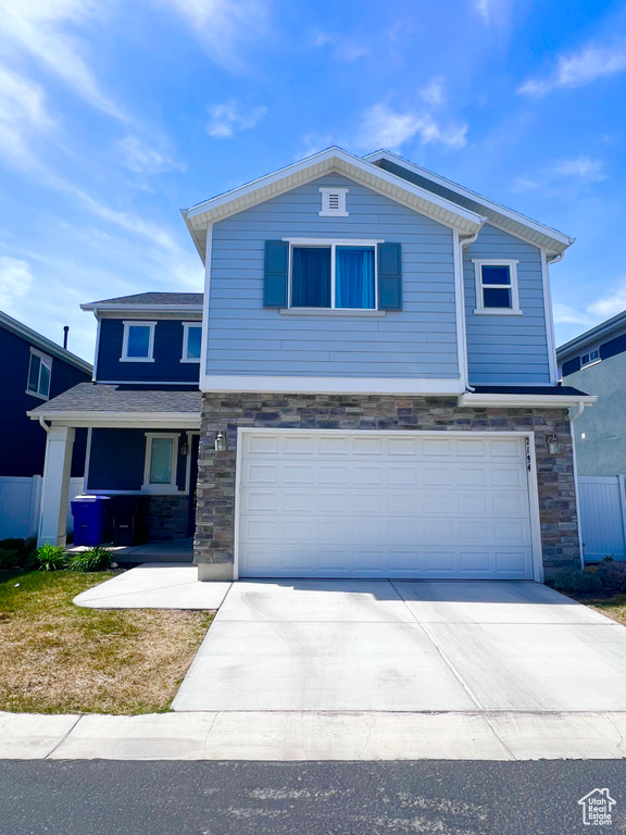 Traditional-style house featuring concrete driveway, an attached garage, fence, and stone siding
