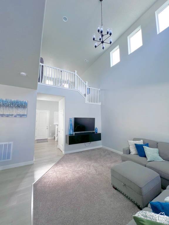 Living area featuring visible vents, a towering ceiling, wood finished floors, baseboards, and a notable chandelier