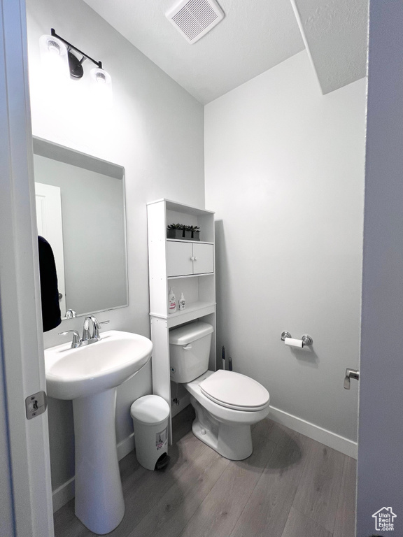 Half bathroom featuring visible vents, wood finished floors, toilet, baseboards, and a sink
