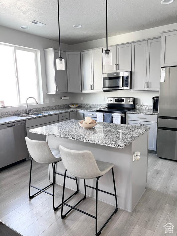 Kitchen with a breakfast bar area, a textured ceiling, appliances with stainless steel finishes, a sink, and gray cabinetry