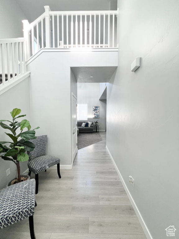 Hall featuring baseboards, light wood finished floors, and a towering ceiling