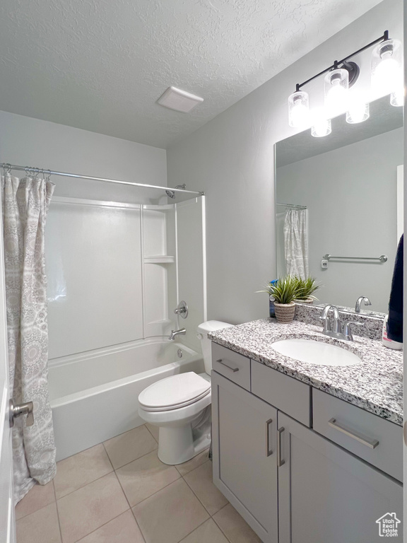 Full bathroom featuring tile patterned flooring, vanity, toilet, a textured ceiling, and shower / bath combination with curtain