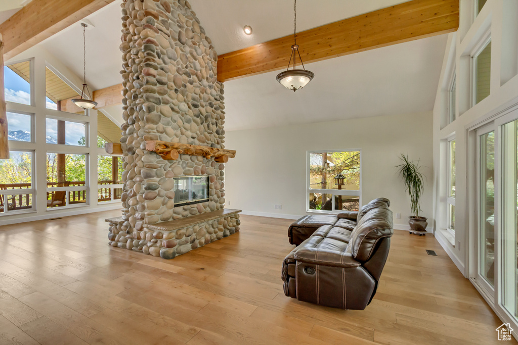 Living room with high vaulted ceiling, a stone fireplace, baseboards, wood finished floors, and beamed ceiling