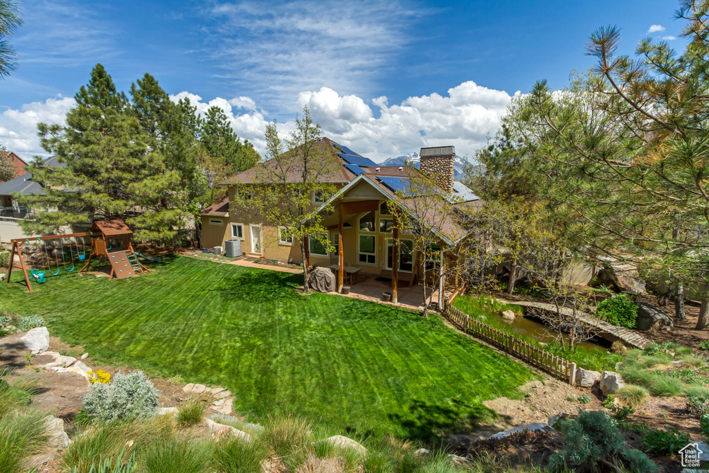 Back of house with a patio, a chimney, a playground, a lawn, and solar panels