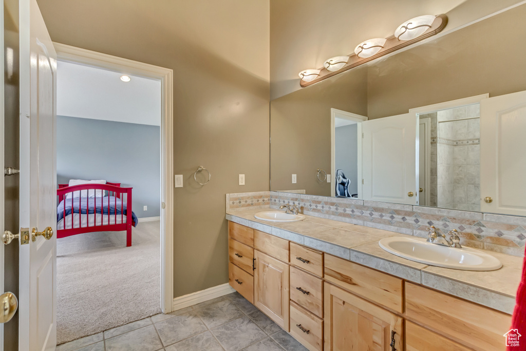 Ensuite bathroom featuring double vanity, a sink, baseboards, and tile patterned flooring