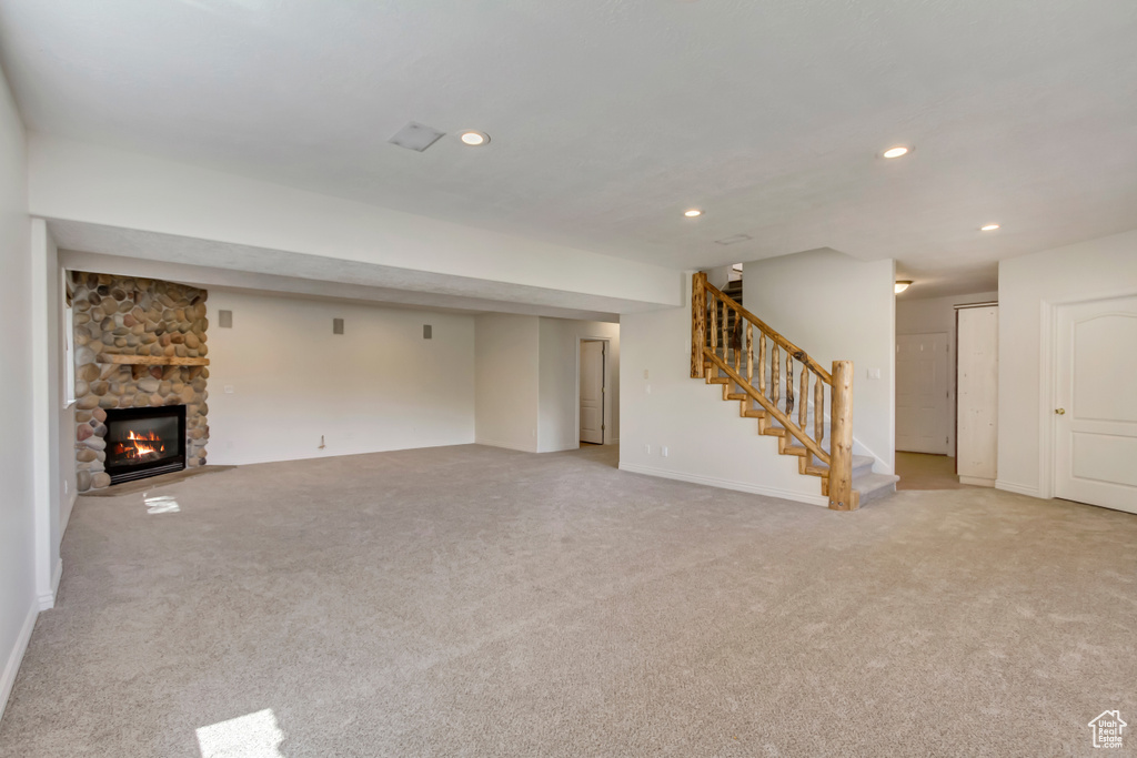 Unfurnished living room featuring stairway, recessed lighting, a stone fireplace, and light colored carpet