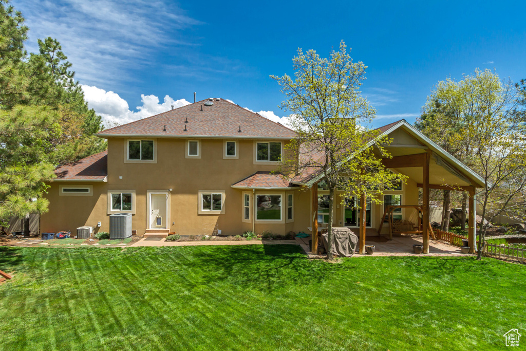 Back of property with central AC unit, stucco siding, and a yard