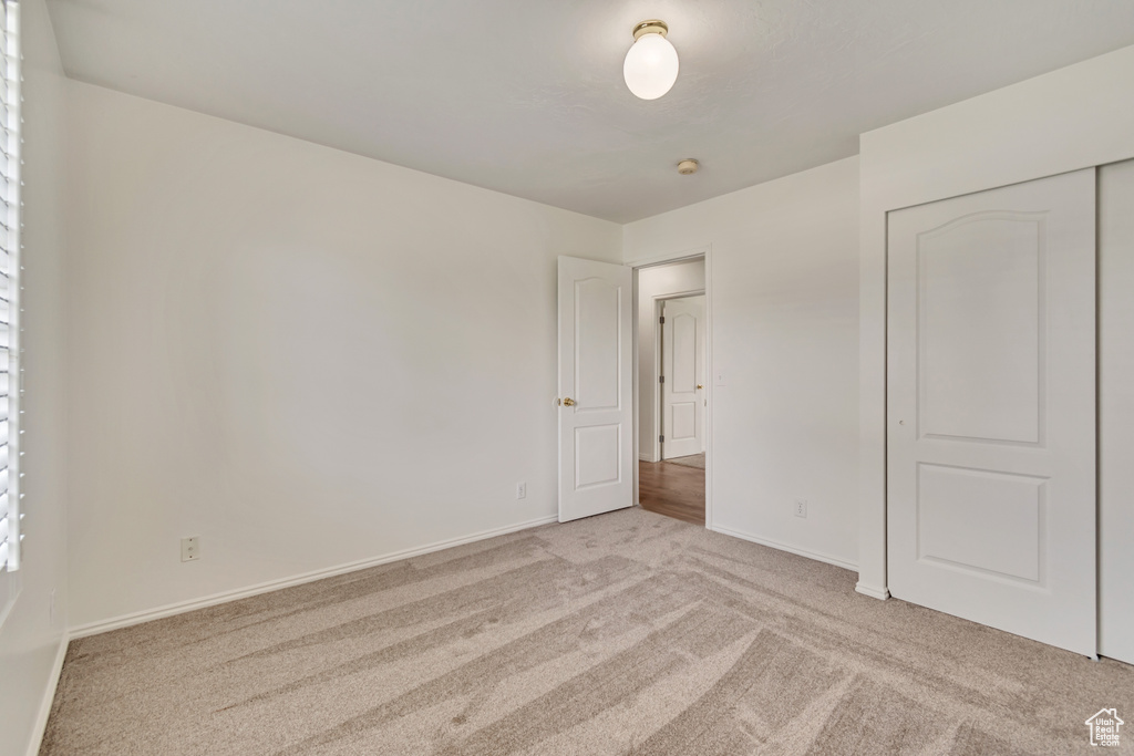 Unfurnished bedroom featuring baseboards, light colored carpet, and a closet
