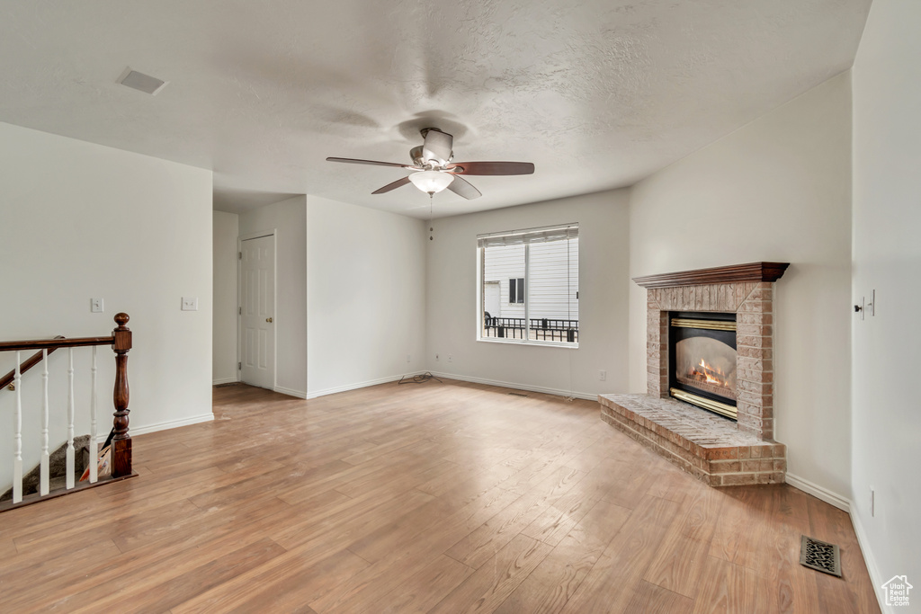 Unfurnished living room featuring light wood finished floors, a fireplace, a ceiling fan, baseboards, and visible vents