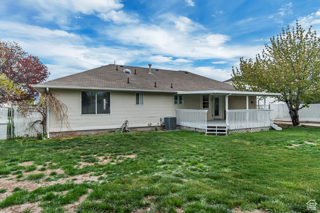 Rear view of house featuring roof with shingles, a lawn, a wooden deck, central air condition unit, and fence