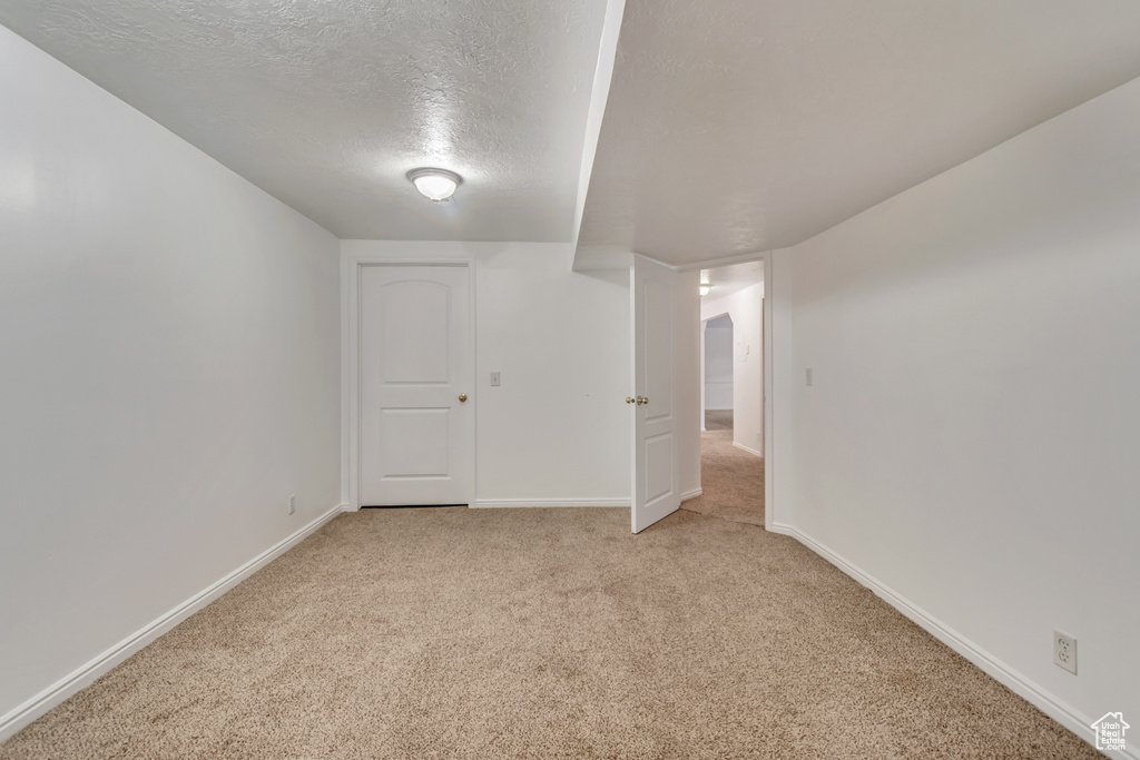 Basement featuring baseboards, a textured ceiling, and light carpet
