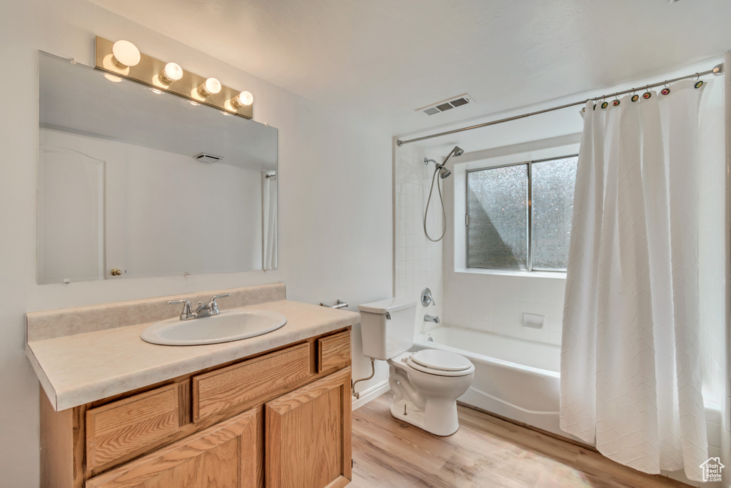 Full bath with visible vents, vanity, wood finished floors, toilet, and shower / bath combo