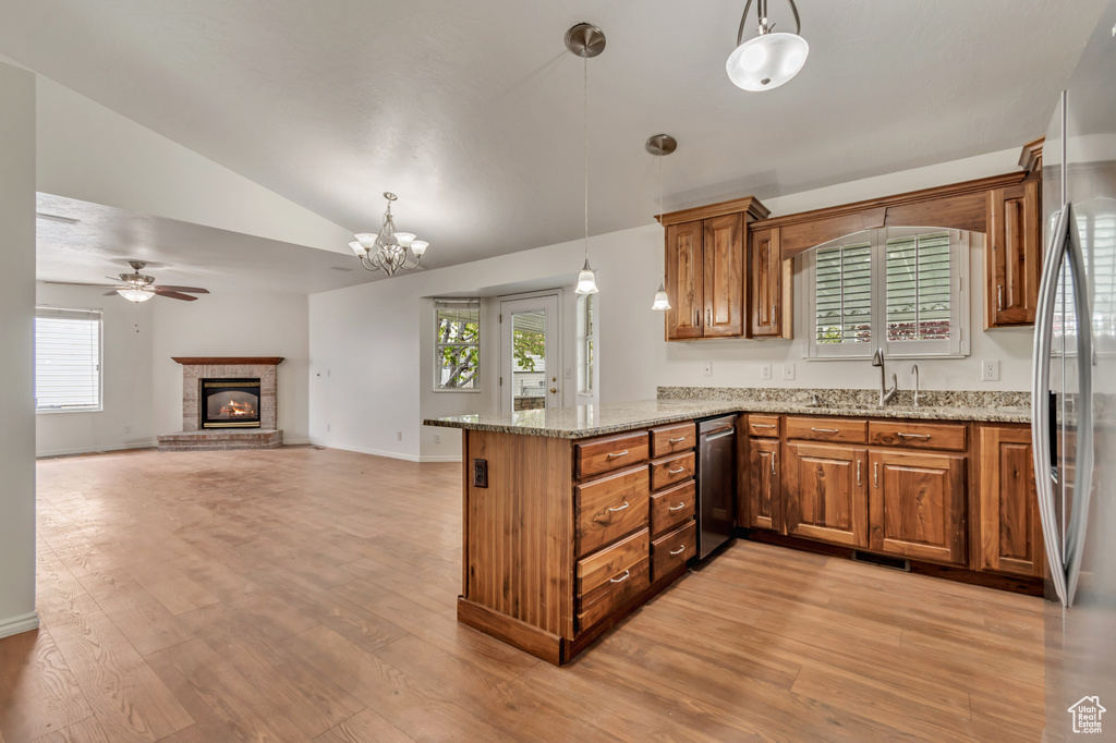 Kitchen featuring a fireplace, vaulted ceiling, brown cabinets, a peninsula, and stainless steel appliances