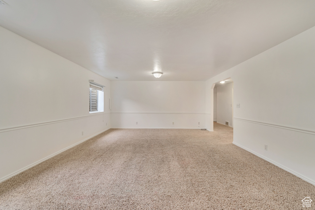 Unfurnished room featuring arched walkways, baseboards, and light colored carpet