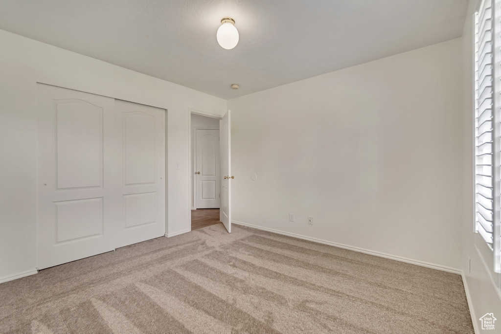 Unfurnished bedroom featuring baseboards, light colored carpet, and a closet