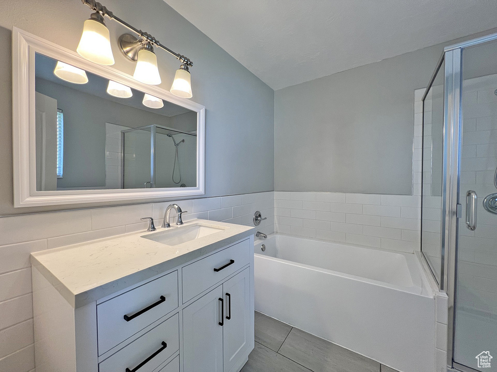 Bathroom featuring vanity, a stall shower, a bath, and tile walls