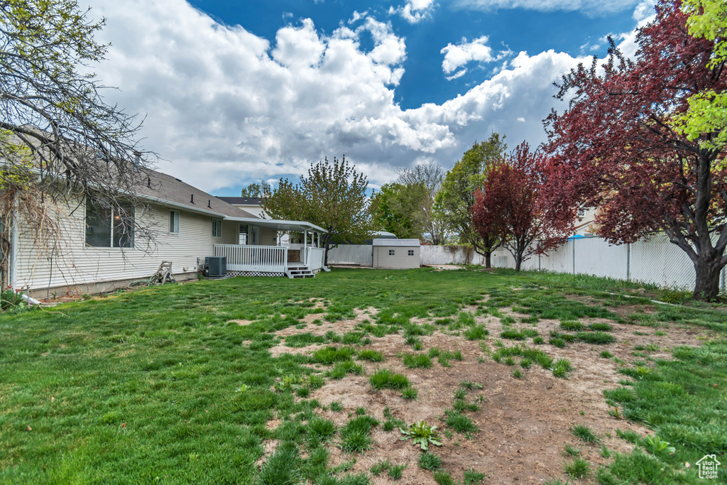 View of yard featuring a wooden deck, central AC unit, an outdoor structure, a fenced backyard, and a shed