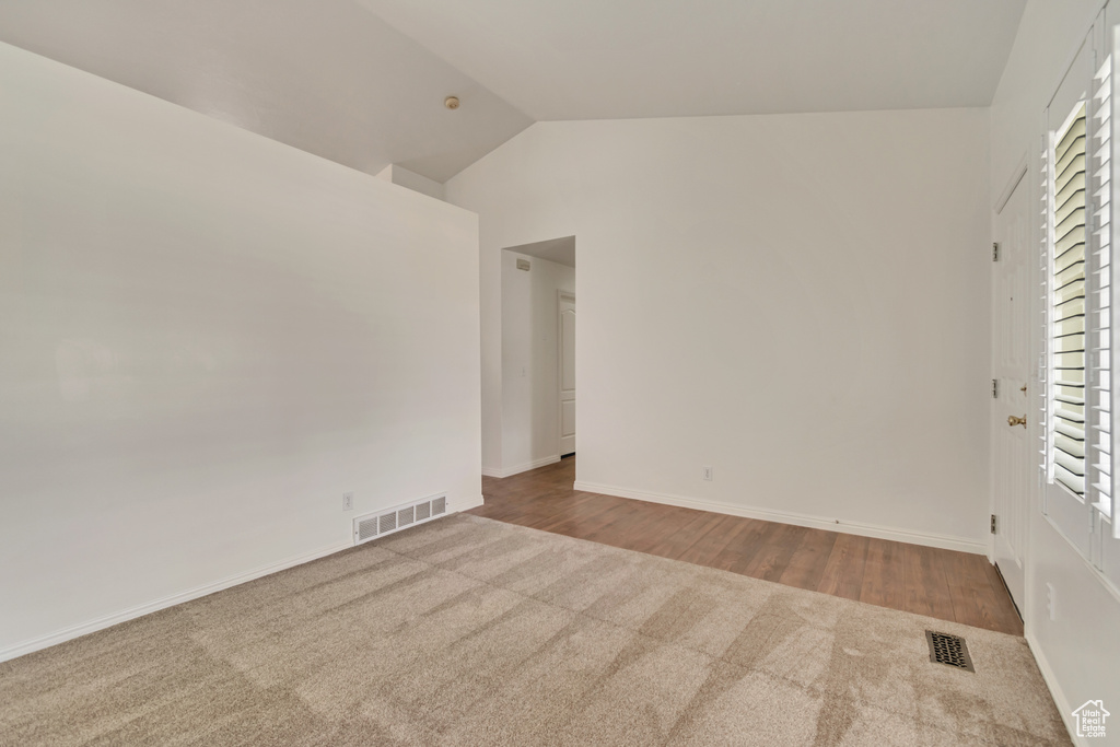 Spare room with carpet floors, plenty of natural light, vaulted ceiling, and visible vents