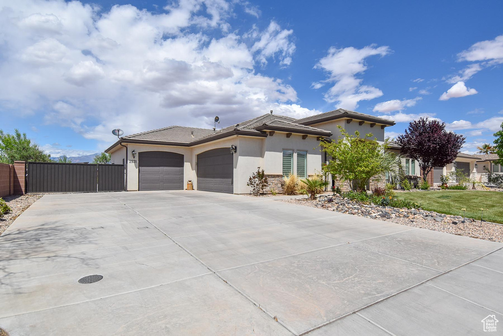 View of front of home featuring a tiled roof, a gate, concrete driveway, an attached garage, and stucco siding