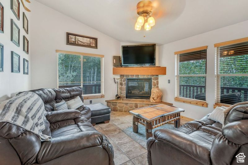 Tiled living room with a fireplace, a ceiling fan, and lofted ceiling