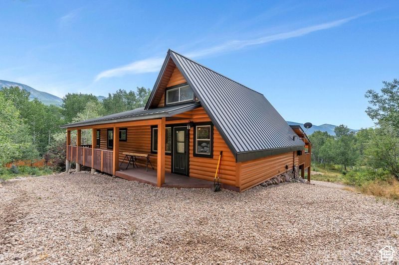 Rear view of house featuring covered porch, log veneer siding, metal roof, and a mountain view