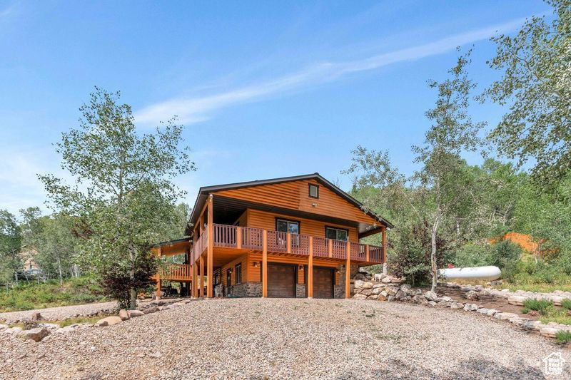 Chalet / cabin featuring log veneer siding, a wooden deck, gravel driveway, an attached garage, and stone siding