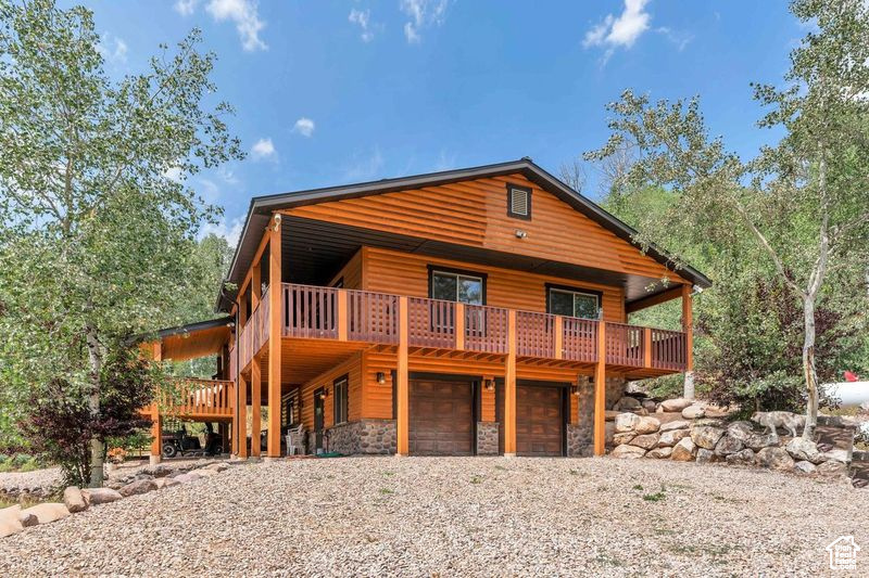 Chalet / cabin with a wooden deck, stone siding, faux log siding, an attached garage, and driveway