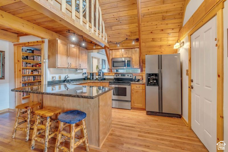 Kitchen with appliances with stainless steel finishes, wooden ceiling, light wood-type flooring, a kitchen bar, and beamed ceiling
