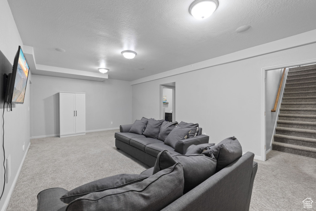 Living room featuring baseboards, a textured ceiling, stairs, and light colored carpet