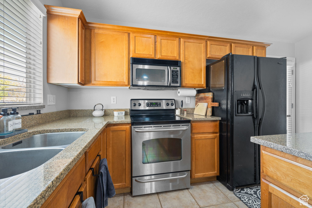 Kitchen featuring stainless steel appliances, a sink, brown cabinets, and light tile patterned floors