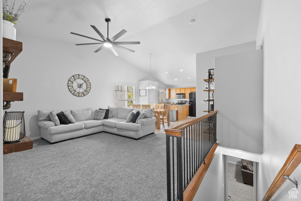Living area with recessed lighting, lofted ceiling, baseboards, light colored carpet, and ceiling fan with notable chandelier