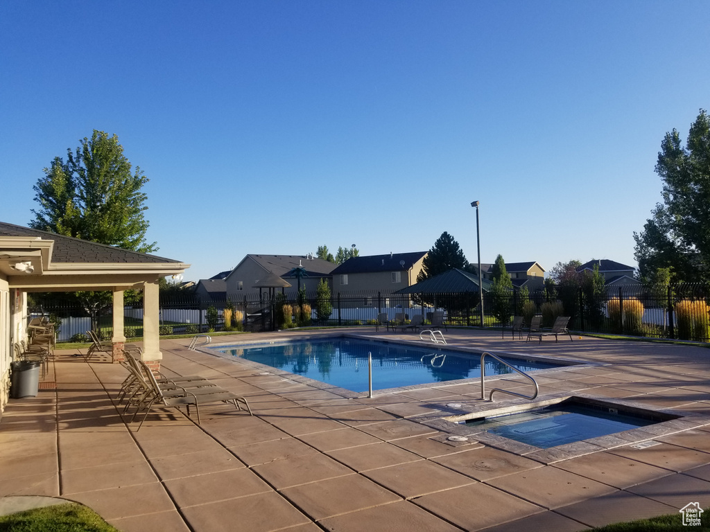 Community pool with a hot tub, fence, a patio area, and a residential view