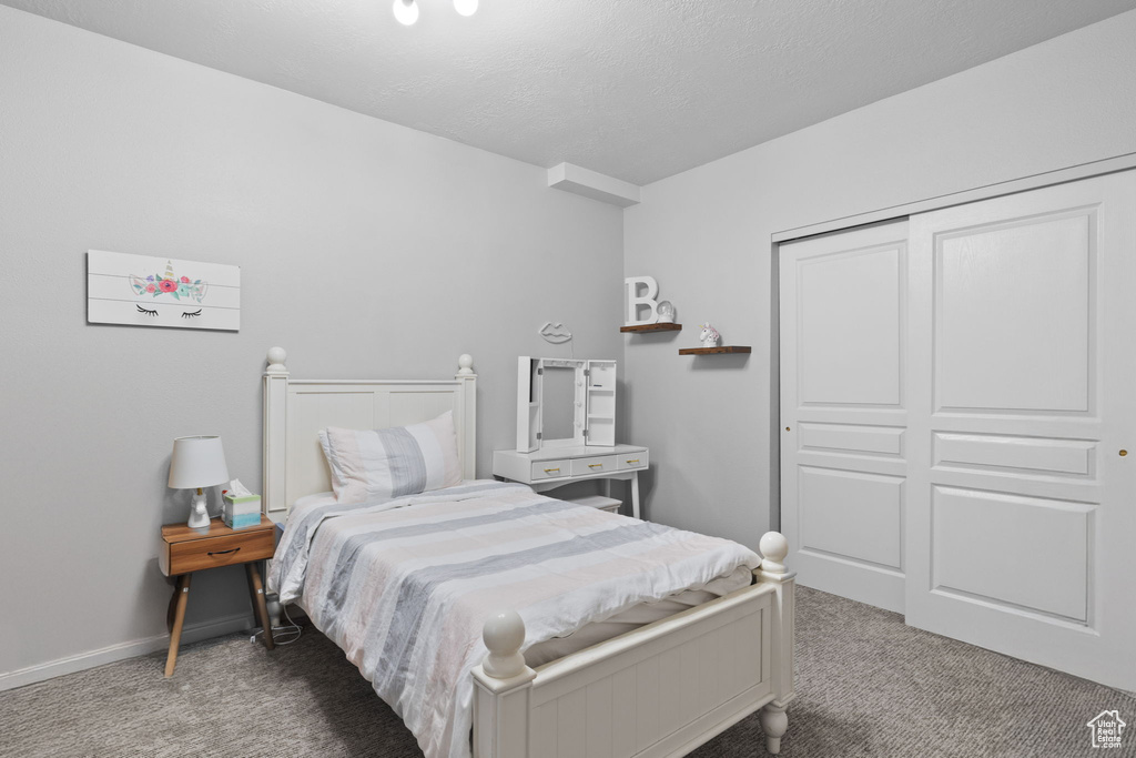 Carpeted bedroom with a textured ceiling, a closet, and baseboards