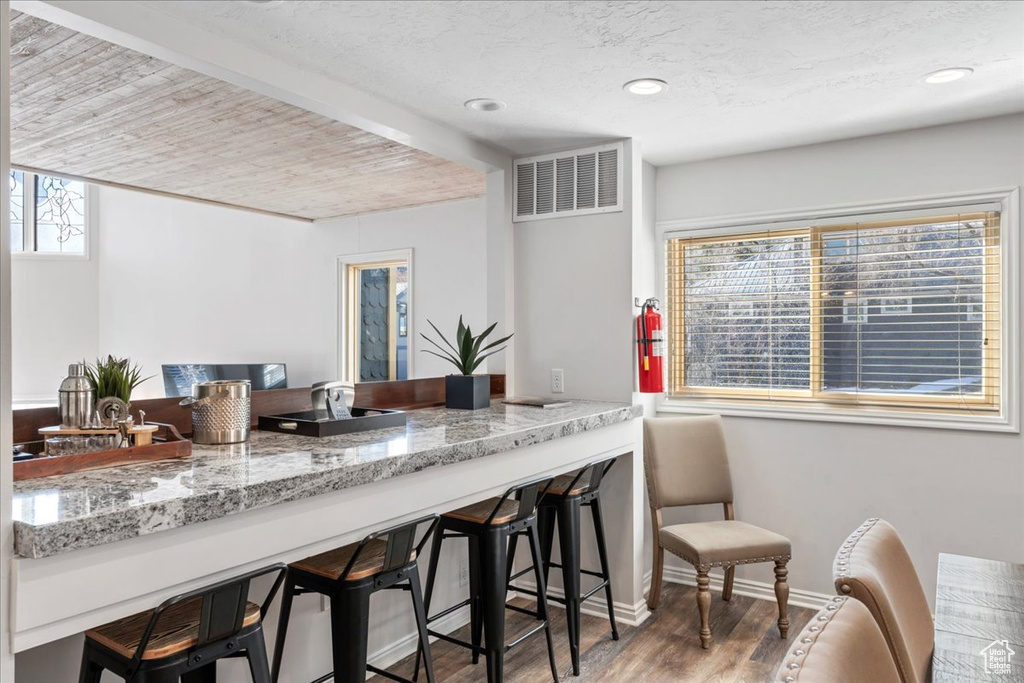 Kitchen with light stone countertops, visible vents, a breakfast bar, and wood finished floors