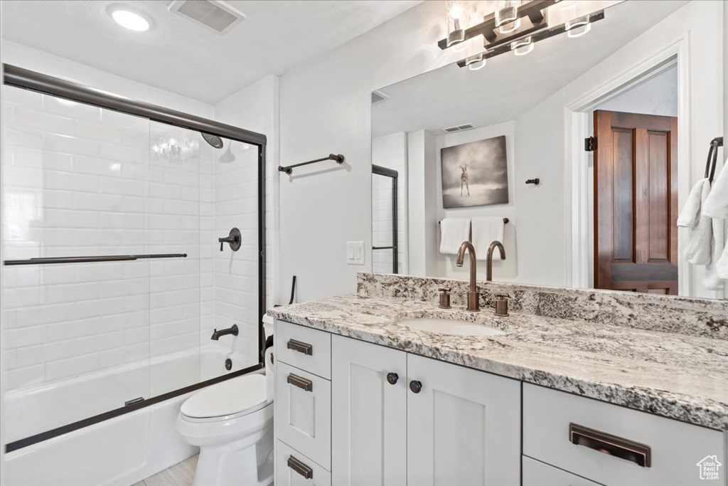 Bathroom with vanity, combined bath / shower with glass door, toilet, and visible vents