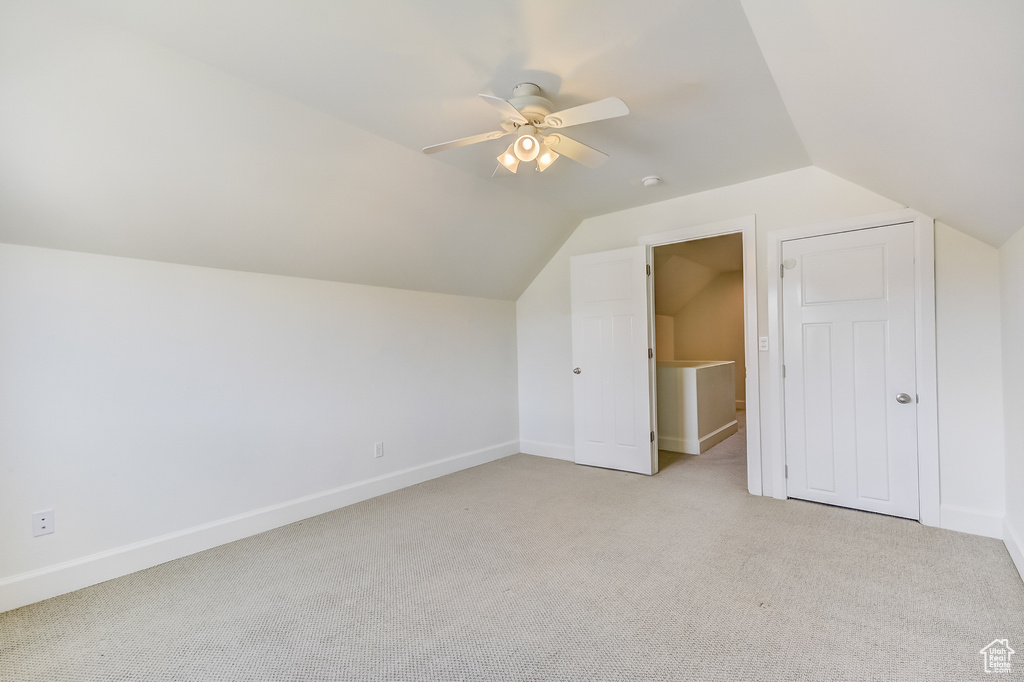 Additional living space with light colored carpet, ceiling fan, vaulted ceiling, and baseboards