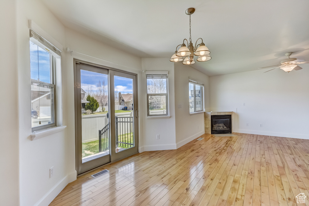Unfurnished living room featuring a tiled fireplace, baseboards, an inviting chandelier, and light wood-style flooring