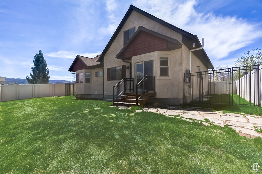 Back of house with a fenced backyard, stucco siding, and a lawn