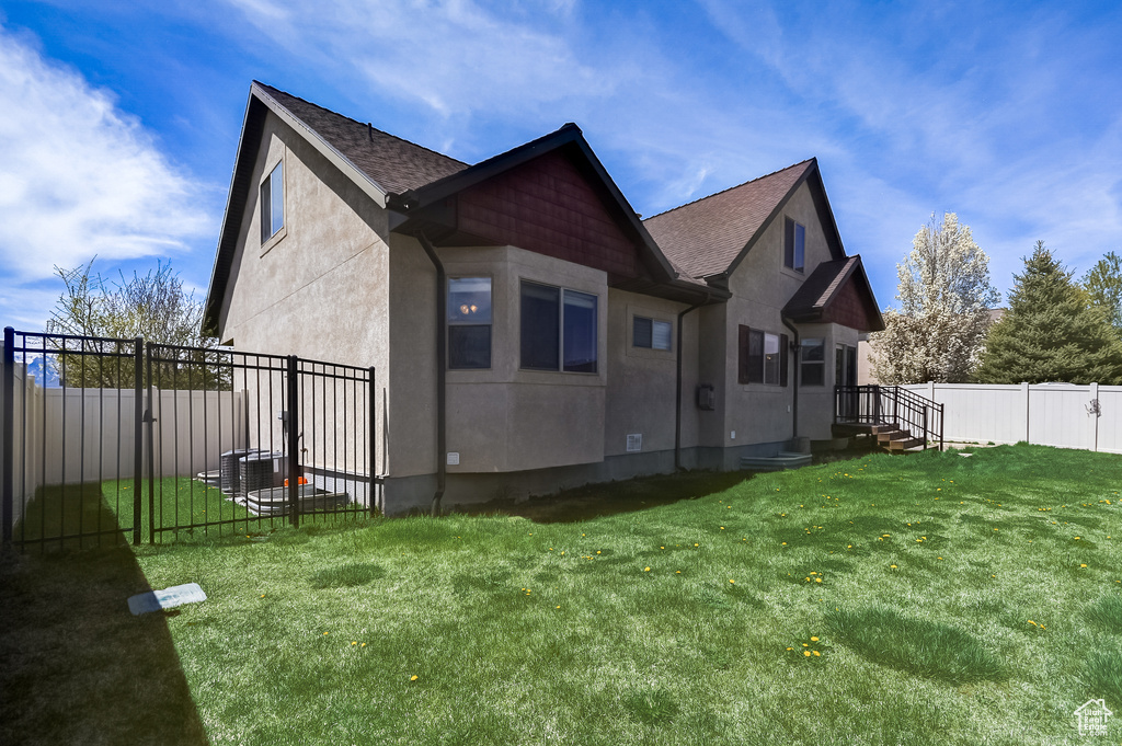 Back of house featuring stucco siding, roof with shingles, a yard, and a fenced backyard
