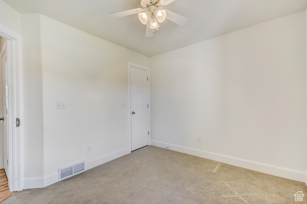 Unfurnished room with a ceiling fan, visible vents, light colored carpet, and baseboards