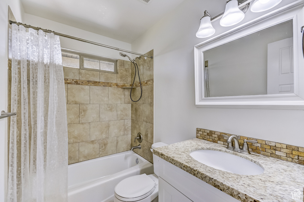 Bathroom featuring shower / bath combination with curtain, toilet, and vanity