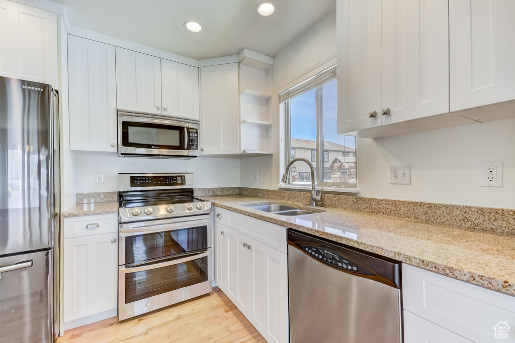Kitchen featuring white cabinetry, stainless steel appliances, light wood finished floors, and a sink