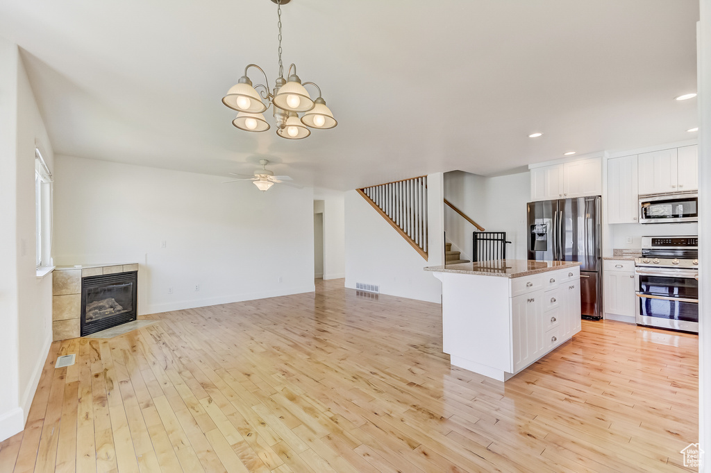 Kitchen with ceiling fan with notable chandelier, white cabinetry, stainless steel appliances, and light wood-style floors