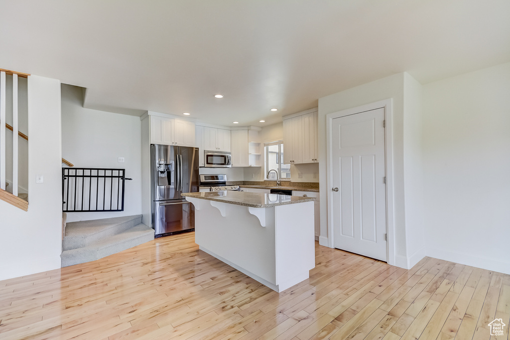 Kitchen with white cabinetry, stainless steel appliances, a kitchen island, and light wood finished floors