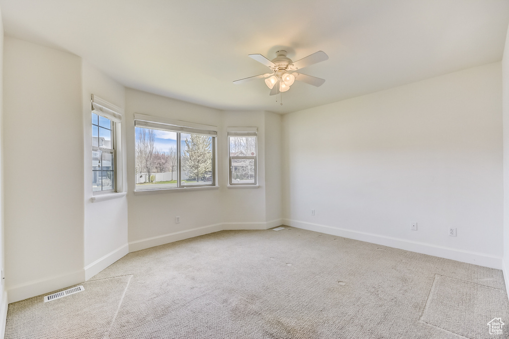 Carpeted empty room with a ceiling fan, visible vents, and baseboards